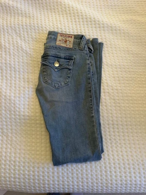 True Religion Joey Low Rise Flare Jeans - Snygga blå jeans från True Religion, modell Joey Low Rise Flare. Jeansen har låg midja, utsvängda ben och detaljerade fickor med knapp bak. Benen är uppsydda och passar någon som är 160 ungefär😊