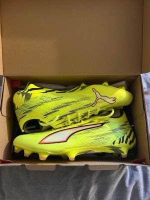 Gula Puma elite fotbollsskor med svart mönster - Säljer ett par riktigt snygga fotbollsskor från Puma i neon-gult med svarta och vita detaljer samt coola tigerinspirerade mönster på hälen. Skorna har låg profil, snörning och är tillverkade i ett lätt syntetmaterial för maxad speed på planen. Det är Puma elite nya kollektion och gräs dubbar. Skorna är aldrig använda därför 10/10 i skick.  Nypris 2799kr från sportringen. 