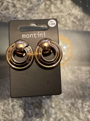 Guldfärgade ringörhängen Montini - Snygga örhängen från Montini i guldfärgad metall. De har en modern, rund design med dubbla ringar som ger ett trendigt intryck. Perfekta för att lyfta vilken outfit som helst med en touch av guld och stilren form.
