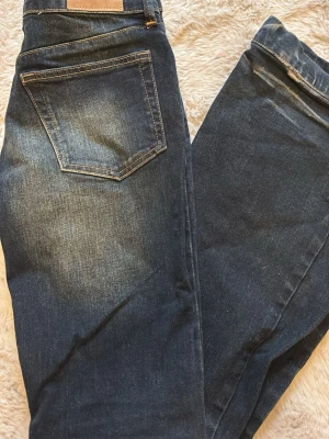 Bootcut jeans från Weekday, mörkblå - Säljer ett par mörkblå bootcut jeans från Weekday med snygga slitningar framtill. Jeansen har klassisk femficksdesign, dragkedjegylf och är tillverkade i denim. Perfekta för dig som gillar en retroinspirerad look med utsvängda ben.