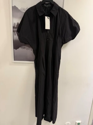 Svart långklänning med krage - Stilren svart långklänning med klassisk krage och korta ärmar från ZARA , Klänningen har knappar framtill och en avslappnad passform, perfekt för dig som gillar minimalistisk stil. Tillverkad i ett lätt och bekvämt material.