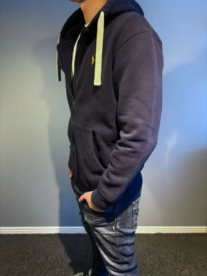 Ralph Lauren hoodie - Mörkblå hoodie från Ralph Lauren med dragkedja, vita snören och den klassiska gula loggan på bröstet. Den har storlek L. 