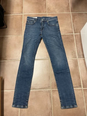 Blåa J.LINEBERG jeans  - Snygga blå jeans med fem fickor. Jeansen har normal midja, dragkedjegylf och kontrastsömmar. Perfekta till en avslappnad stil och funkar året runt. Materialet är denim i bomull med lite stretch för extra komfort. 