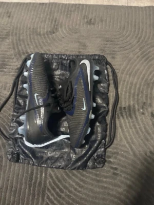 Nike svarta fotbollsskor med blå detaljer - Ett par svart/bebisblåa Nike phantom 6. Storlek 44.5. Har används jätte lite ser ut som helt nya och känns som helt nya. Tvättar såklart dem innan jag skickar iväg dem. Pris kan diskuteras privat!!!