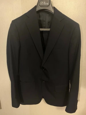 Kostymset - Oscar Jacobson - Ett snyggt mörkblått kostymset från Oscar Jacobson | Storlek: 46 | skick: Mycket bra, liten defekt på bild 7(byxan) | Perfekt inför finare tillställningar |Frågor? Kom privat!