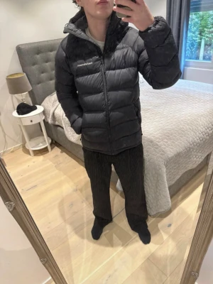 Svart pufferjacka från Peak Performance - Säljer en svart pufferjacka från Peak Performance med hög krage och dragkedja framtill. Jackan har en klassisk quiltad design och är vadderad för extra värme. Perfekt för kalla dagar och har en stilren look som passar till det mesta.