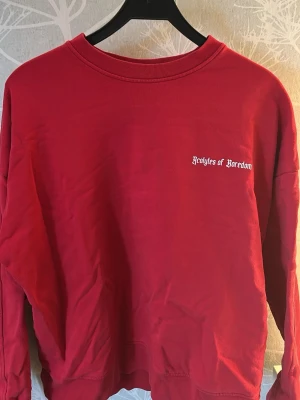 Röd sweatshirt - Röd sweatshirt med vit text på bröstet och stor tryckt text på ryggen. Tröjan har rund halsringning, långa ärmar och ribbade muddar. 