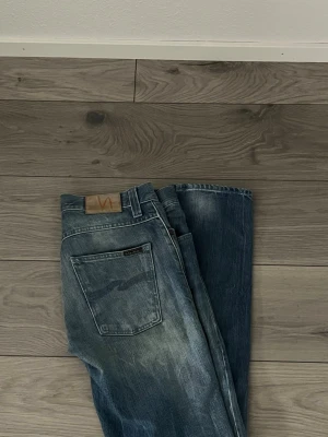 Blå jeans från Nudie Jeans - Säljer ett par klassiska blå jeans från Nudie Jeans med snygg slitning och raka ben. Jeansen har fem fickor, normal midja och är gjorda i denim med en cool tvättad look. Perfekta för en avslappnad stil. 