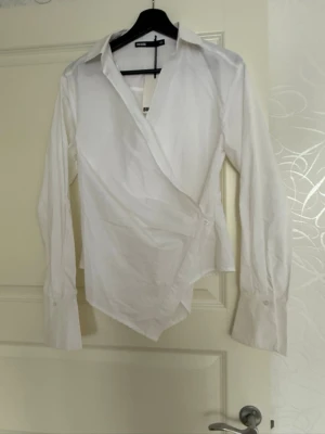 Vit omlottblus från Bik Bok - Säljer en stilren vit skjorta från Bik Bok med lång ärm och klassisk krage. 