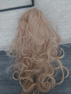 Lång lockig blond cosplayperuk - Säljer en lång och lockig blond peruk perfekt för maskerad eller cosplay. Peruken har mjuka, voluminösa lockar och är tillverkad av syntetiskt material. Passar dig som vill ha ett dramatiskt och coolt hår till din outfit.