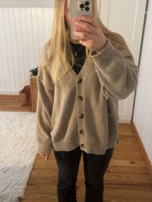 Beige oversized kofta med knappar - Mysig beige oversized kofta med stora knappar framtill och ribbade muddar vid ärmslut och nederkant. Koftan har en avslappnad passform och är perfekt att slänga på sig över en t-shirt eller topp. OBS : jag har syt ihop slitsen på koftan, se bild 5. 