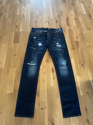 Dsquared2 jeans - Säljer ett par mörkblå jeans med slitningar och distressed detaljer framtill. Jeansen har raka ben, klassisk femficksmodell och kontrastsömmar. Perfekta för en avslappnad och trendig look. Nypris ca 4000. Pris kan diskuteras vid snabb affär. Fråga gärna vid funderingar.