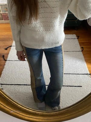 Utsvängda Blå lågmidjade jeans med beige paneler - Unika blå jeans med breda beige paneler längs sidorna och bakficka. Jeansen har utsvängda ben och en cool kontrast mellan denim och manchestertyg. Perfekta för dig som vill sticka ut med din stil.