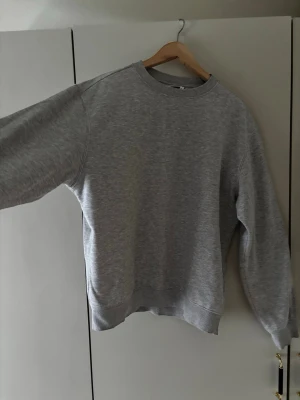 Grå sweatshirt från Weekday - En klassisk grå sweatshirt från Weekday med sopassande relaxed fit och rund halsringning. Tillverkad i mjuk bomullsblandning och har ribbade muddar vid ärmslut och tips cover. Perfekt för en chill och enkel stil. Nypris 400kr
