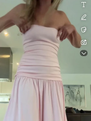 Ljusrosa axelbandslös klänning - Supersöt ljusrosa klänning med axelbandslös design och smockad överdel. Kjolen är vid och faller mjukt ner till knäna. Super fin klänning som passar perfekt till sommarens alla tillfällen eller balen. Klänningen är endast testad! Storlek xs  