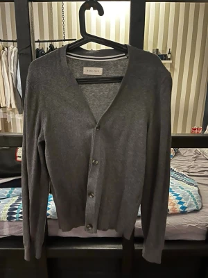 kofta från Pier One - Stilren mörkgrå kofta från Pier One med v-ringning och knäppning framtill. Långärmad modell i tunt, mjukt material som passar perfekt för lager på lager. Klassisk och enkel design som funkar till det mesta.