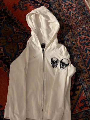 Archive Number (N)ine Skulls Zip-up - Säljer nu min vita Number (N)ine zip-up hoodie med de ikoniska broderade skallarna. Plagget har en klockren arkiv-estetik med fabriksgjord "distressing" (små hål och slitningar) som är karaktäristiskt för märket och Takahiro Miyashitas design. Väldigt skön kvalitet med en rymlig huva och våfflad textur på insidan. Notera att denna modell har en stilren design utan fickor på framsidan.  (Storlek 1 Passar som en Small) 