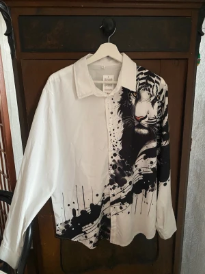 Vit skjorta med svart tigermotiv - Unik vit skjorta med svart konstnärligt tigermotiv och stänkmönster på ena sidan. Klassisk krage och långärmad modell. Perfekt för dig som vill sticka ut med en kreativ och cool look. (möts upp i Stockholm)
