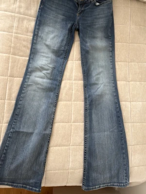 Blå bootcut jeans från Nudie Jeans - Säljer ett par blå bootcut jeans från Nelly. Jeansen har en ljus tvätt och markerade sömmar, samt ett broderat 'N' på bakfickan. 