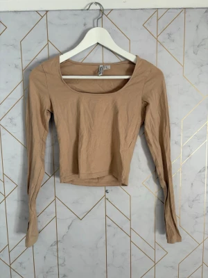 Beige croppad långärmad topp H&M - Trendig beige croppad topp från H&M med lång ärm och bred, rundad urringning. Tillverkad i mjuk bomull som känns skön mot huden. Perfekt att styla med höga jeans eller kjol för en clean look.