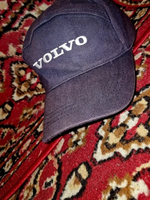 Svart keps med Volvo-logga - Snygg svart keps med broderad VOLVO-logga i vitt framtill. Klassisk böjd skärm och justerbar passform bak. Tillverkad i slitstarkt bomullstyg, perfekt för dig som gillar bilar och vill ha en stilren accessoar.