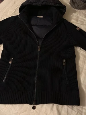 Moncler cardigan (Äkta) - Snygg svart stickad jacka från Moncler med huva och dragkedja framtill.  Passar både M och L dene liten i storleken