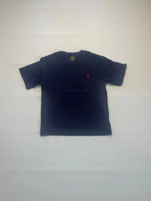 Mörkblå t-shirt från Polo Ralph Lauren storlek S - Klassisk mörkblå t-shirt från Polo Ralph Lauren med korta ärmar och rund halsringning. T-shirten har en liten röd broderad logga på bröstet och är tillverkad i mjuk bomull för en skön känsla. T-shirten är i storlek S, är helt ny och aldrig buren