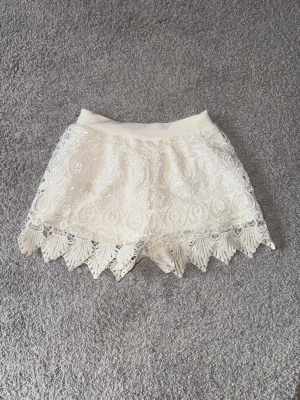 Vita spetsiga shorts  - Snygga vita shorts med spets och dekorativ kant nertill. De har elastisk midja och är 