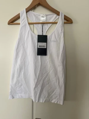 Vit linnetopp från ICANIWILL - Snygg vit linnetopp från ICANIWILL med brottarrygg och diskret logga på bröstet. Perfekt för träning eller chill dagar. Enkel och stilren design som passar till allt.