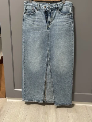 Lång jeanskjol med slits från Levi's - Snygg lång jeanskjol från Levi's i klassisk ljusblå denim. Kjolen har fem fickor, hällor för bälte och en tydlig slits framtill för extra rörelsefrihet. Perfekt till sneakers eller boots för en cool vardagslook.