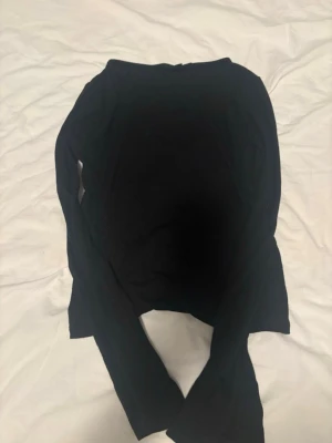 Svart långärmad topp - En stilren svart långärmad topp med enkel design. Toppen har rund halsringning och är tillverkad i ett mjukt material som känns skönt mot huden. Perfekt att matcha med jeans eller kjol för en clean look. Har slits vid armarnas slut. 