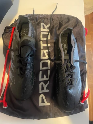 Adidas Predator svarta fotbollsskor - Snygga svarta Adidas Predator fotbollsskor med silvriga detaljer och klassisk snörning. Skorna har en modern, strömlinjeformad design och är tillverkade i syntetmaterial för bästa grepp och känsla på planen. Levereras med en svart Predator-påse med röda snören. Storlek är fel så gissar mellan 38-40 använda en gång!