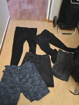 En hel drös jeans och shorts - Parti med svarta byxor och shorts. Innehåller två par svarta jeans[av märket Neuw], ett par svarta shorts och ett par mönstrade shorts. Alla plagg är i mörka nyanser. Camo shortsen är 31 i midjan övriga är 32 i midjemått.