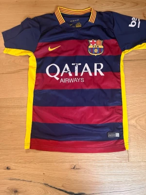 FC Barcelona Neymar Jr matchtröja - Säljer en officiell FC Barcelona matchtröja från Nike med Neymar Jr och nummer 11 på ryggen. Tröjan har breda blå och vinröda ränder, gula detaljer och klubbmärke på bröstet. Materialet är lätt och andas, perfekt för fotbollsträning eller support.