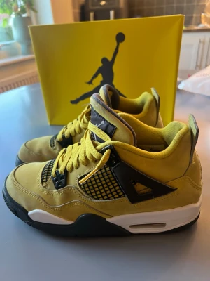 Air Jordan 4 Retro Lightning sneakers - Gula Air Jordan 4 Retro Lightning sneakers med svarta och vita detaljer. Ovandel i mocka och mesh, klassisk siluett med högt skaft och ikoniska Jumpman-loggan på plösen. Skorna har gula skosnören och svart nätpanel på sidorna. Perfekta för dig som vill sticka ut.