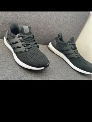 Adidas Ultra Boost svarta sneakers - Svarta Adidas Ultra Boost sneakers med stickad ovandel och klassiska tre ränder i plast på sidorna. Skorna har en vit Boost-sula för extra komfort och en sportig look. Perfekta för dig som gillar stilrena och bekväma sneakers. Helt nya, storlek 42