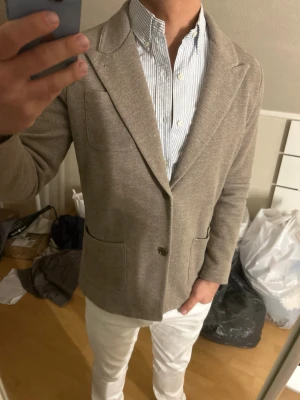 John Henric Beige kavaj med två knappar - Stilren beige kavaj med två knappar framtill och två stora fickor. Klassisk passform med mjuk struktur och smala slag. Perfekt att matcha med skjorta för en snygg look. Materialet ser ut att vara bomull eller ullblandning. (Knappen nere e lite lös)
