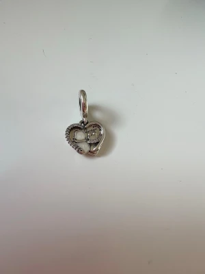 Pandora hjärtberlock i silver - Söt hjärtformad berlock från Pandora i silverfärg med gnistrande stenar runt kanten och detaljer i vitt. Perfekt att hänga på armband eller halsband för en personlig touch. Ordinarie pris är 799kr, jag säljer den för 499kr