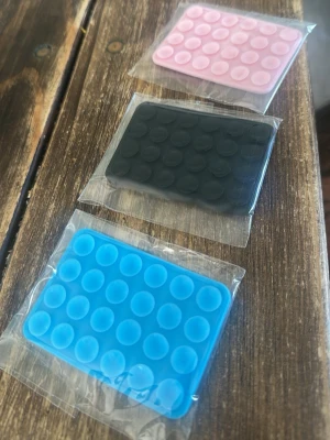 Sugproppsmatta för mobil, 3-pack - Tre rektangulära sugproppsmattor i silikon för mobiltelefoner, i färgerna blå, svart och rosa. Perfekt för att fästa mobilen på släta ytor. Kompakt och flexibel design som enkelt kan tas med i fickan eller väskan.