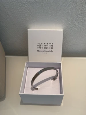 Maison Margiela silverfärgat armband - Stilrent armband från Maison Margiela i silverfärgad metall. Armbandet har en minimalistisk design med ingraverad logotyp på framsidan. Kommer i original ask, perfekt för dig som gillar exklusiva accessoarer med modern känsla.