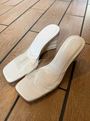 Beiga klackar med transparent rem  - Säljer ett par helt nya oanvända snygga sandaler / klackar från Senso köpa på New Yorker med beige sula och kilklack i flätad jute. De har en modern fyrkantig tå och bred transparent rem över foten. Perfekta för en trendig sommarlook och lätta att matcha med olika outfits. Dom är i storlek 40 men passar 39! Små i storlek.