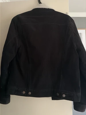 Svart jeansjacka med teddyfoder H&M XS - Svart jeansjacka från H&M L.O.G.G. i storlek XS. Jackan har mjukt vitt teddyfoder på insidan och vid kragen, klassisk jeansjackemodell med knappar nertill och på ärmsluten. Perfekt för dig som gillar en stilren och bekväm look.
