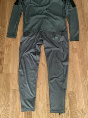 Nike dri fit  - Säljer ett grått träningsset från Nike med långärmad tröja och matchande byxor. Setet är gjort i ett mjukt och stretchigt funktionsmaterial, perfekt för träning. Byxorna har dragkedjor vid bensluten och Nike-logga på låret. Snygg och sportig look!
