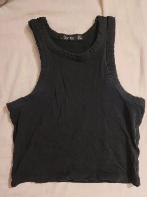 Svart cropped linne från Boohoo - Säljer ett svart cropped linne från Boohoo med breda axelband och rund halsringning. Perfekt till jeans eller kjol för en avslappnad och trendig look. Tillverkat i mjuk bomull som känns skön mot huden.