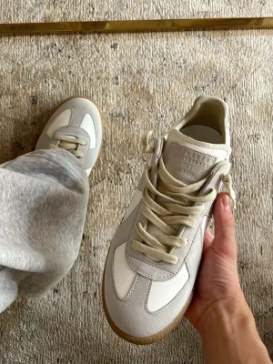 Maison Margiela Gats Vit/grå  - Riktigt fina gats ifrån Maison Margiela. Perfekt sko inför sommaren med dess snygga detaljer. Materialet är läder och mocka med en brun sula (se bilder) För små för mig tyvärr men passar dig med storlek 43-44. Box ingår självklart😀😀Vid frågor kom DM😄Pris går att diskutera