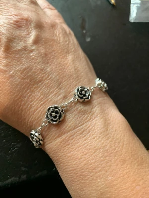 Silverfärgat armband med blommor - Snyggt armband i silverfärg med detaljerade blommor som länkar. Armbandet har en klassisk kedja och varje blomma är fint utformad i metall. Perfekt accessoar för dig som gillar unika och stilrena smycken.