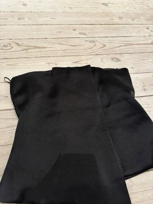 Svart satin bandeau tubtopp - Snygg svart bandeau tubtopp i satinliknande material. Toppen är axelbandslös. Lite korsettliknande vibe!