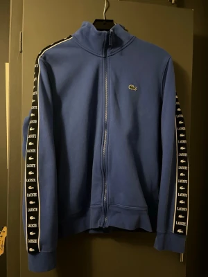 Blå zip-hoodie från Lacoste - Säljer min Lacoste hoodie som är nyköpt men var tyvärr lite stor. Den är nyskick så säljer den för de priset jag köpte den för till och börja med. Priset kan diskuteras🩷