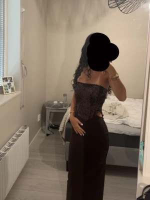 Brun långklänning med paljetter - Snygg brun långklänning med glittrig paljettöverdel och axelbandslös design. Klänningen har figurnära passform och en elegant, rak siluett. Perfekt för dig som vill sticka ut med en trendig och stilren look.