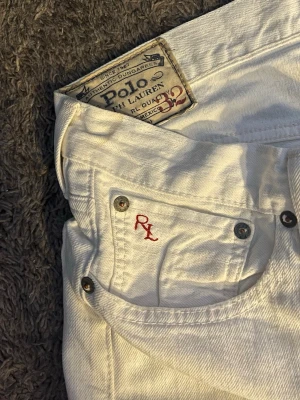 Vita jeans från Polo Ralph Lauren - Snygga vita jeans från Polo Ralph Lauren med klassisk femficksdesign och röd RL-brodering på myntfickan. Jeansen har raka ben och är tillverkade i kraftig denim. Perfekta för en clean och fräsch look. Det finns fläckar på jeansen därför priset är så lågt, dom borde finnas med i bilderna